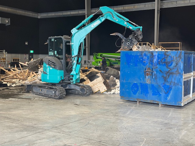 Excavator loading demolition debris into a skip